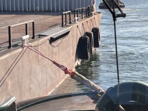 Close-up of a marine vessel tied to a dock with ropes and fenders in port.
