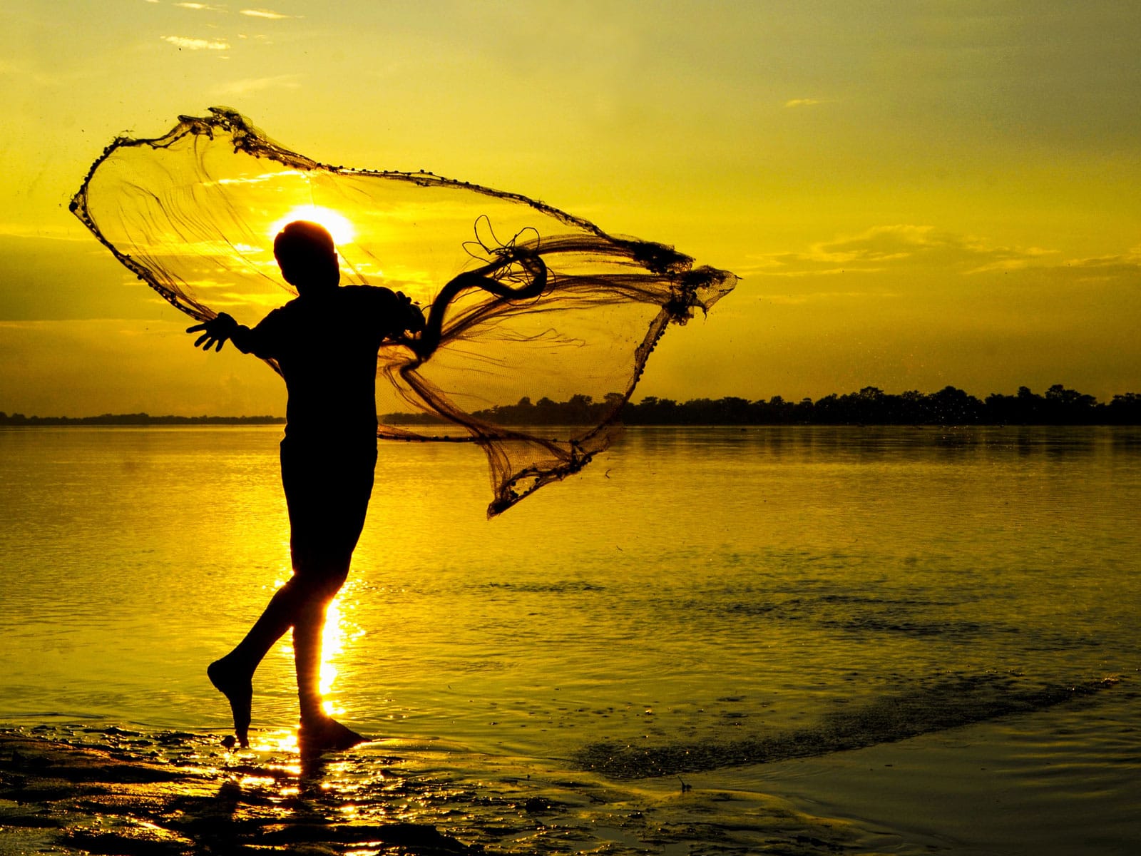 Child playing with fishing net by the water at sunset, scenic outdoor image.