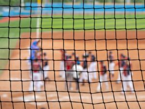 Baseball players on field seen through protective netting during game at Cortland.
