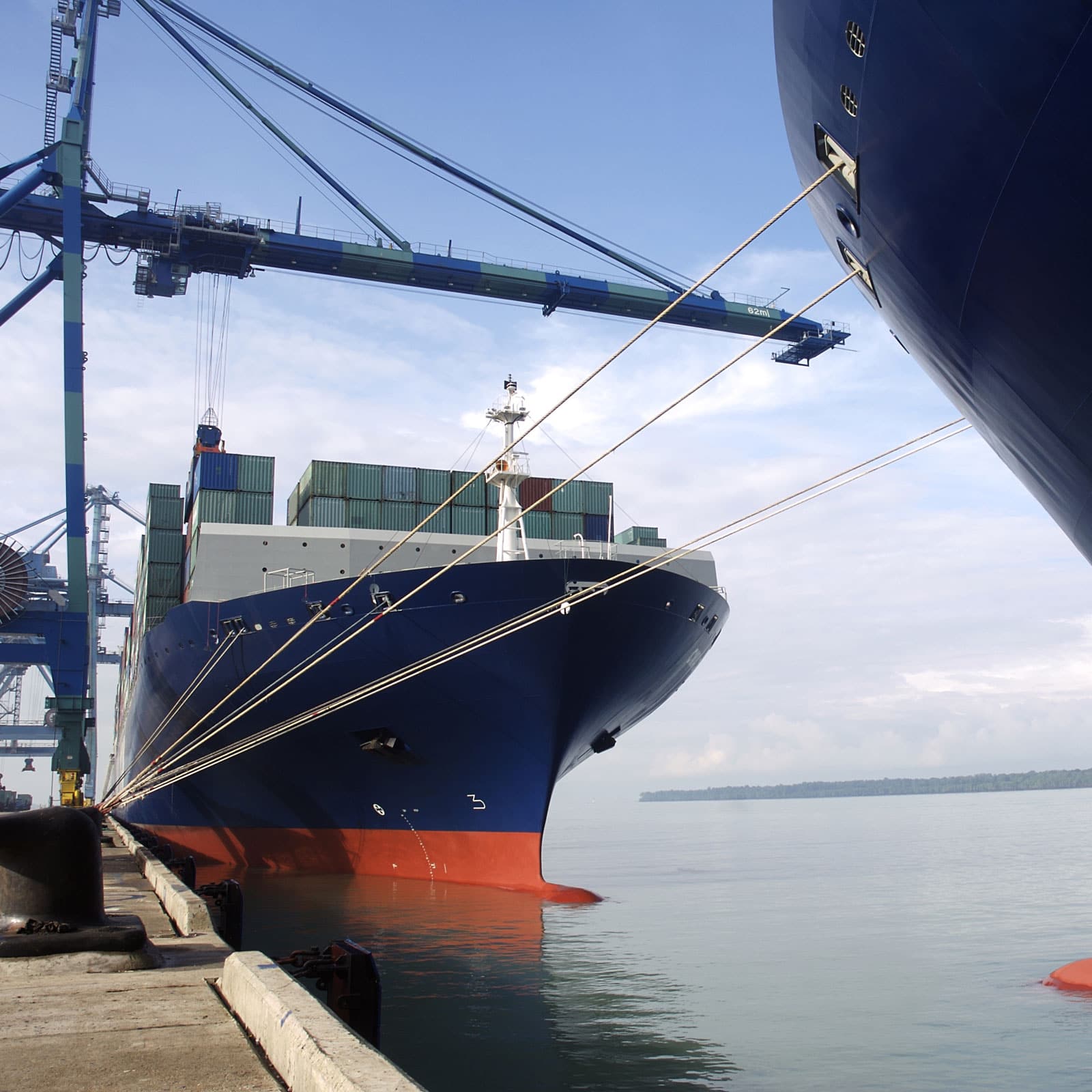 Large cargo ship with containers docked at port with cranes in background.