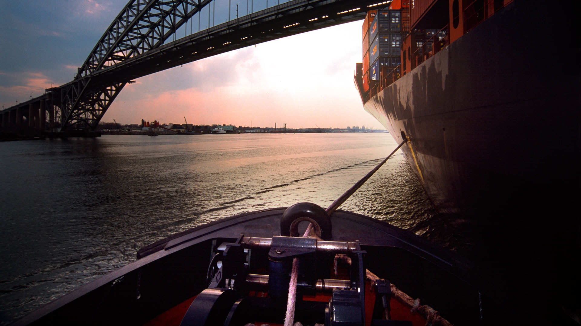 Cargo ship navigating under bridge on water during sunset.