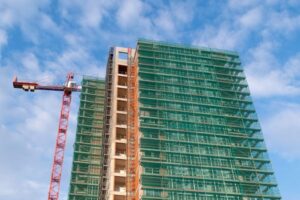 Skyscraper under construction with green safety netting and crane.