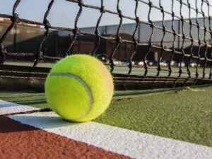 Bright yellow tennis ball near the net on a tennis court.
